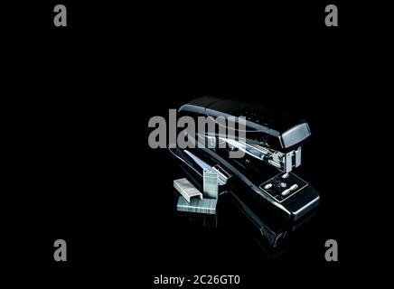 Black stapler and staples on dark background. Stock Photo