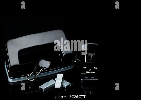 Black stapler, staples, paperclip and punch on dark background with copy space. Office equipment concept Stock Photo