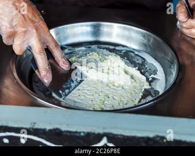Making rolled ice cream. Man hands making kiwi and banana Thay style natural ice cream Stock Photo