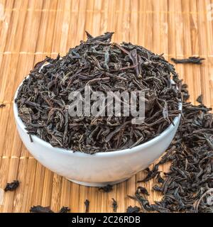 Dried tea is poured into a ceramic cup on a bamboo mat Stock Photo