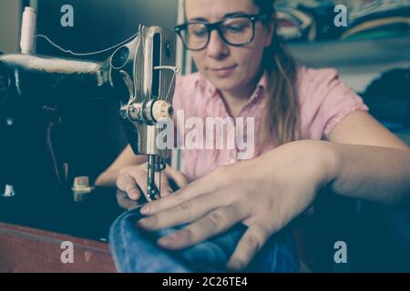 homemaker repairing blue jeans with retro vintage sewing machine at home Stock Photo