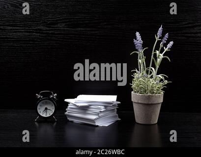 stack of white square note papers, a ceramic pot of lavender and an alarm clock on a black office desk, Scandinavian style Stock Photo