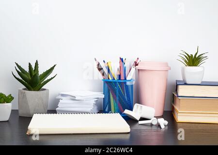 stack of books, spiral notebooks, ceramic cup with coffee and colorful pencils on a black table, work space Stock Photo