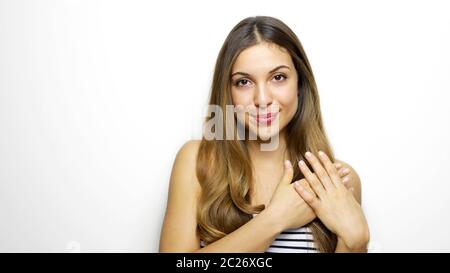 People, kindness and generosity concept. Cheerful young woman keeps hands on heart, expresses cordialty and friendliness, has charming smile, poses ag Stock Photo