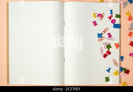 open notebook with white sheets in a cage and small multi-colored wooden letters, back to school, copy space Stock Photo