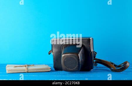 old film camera in a brown leather case on a blue background and rope bound vintage postcards Stock Photo