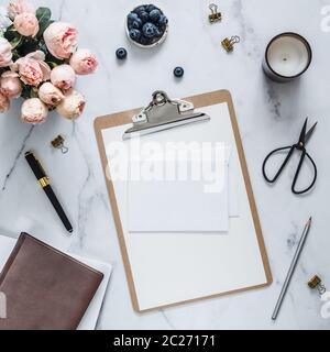 Wedding mock up. Flat lay with blank greeting card, envelope. Clipboard, flowers, scented candle on white marble. Feminine home office mock up with co Stock Photo