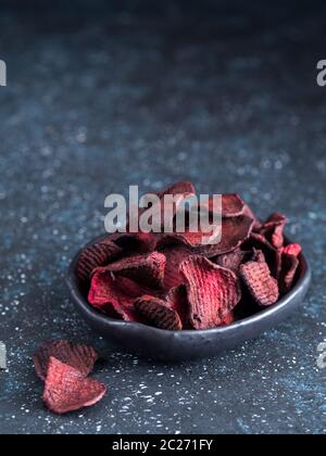 Baked beet slices. Healthy homemade beetroot chips in plate on dark blue background. Copy space Stock Photo
