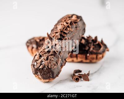 Homemade eclairs with chocolate on white marble background. Close up view of delicious healthy profitroles with chocolate glaze Stock Photo