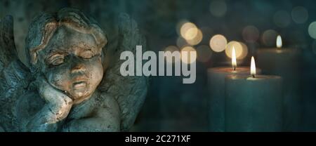 Candles with angel sculpture and golden bokeh on dark background Stock Photo