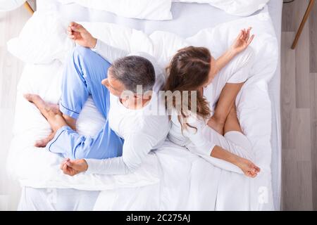 Matured Couple Sitting Back To Back On Bed Meditating Stock Photo