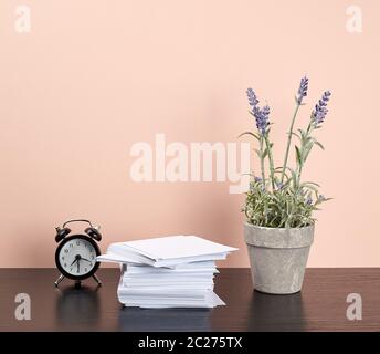 stack of white square note papers, a ceramic pot of lavender and an alarm clock on a black office desk, Scandinavian style Stock Photo