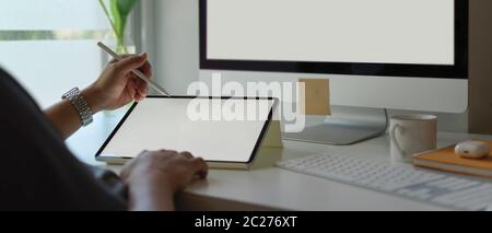 Cropped shot of male entrepreneur working with blank screen tablet and computer on simple office desk beside window Stock Photo