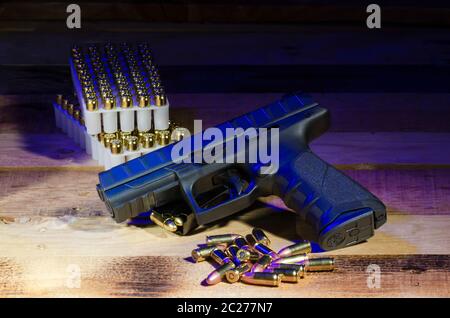 a modern semi automatic weapon rest a top of a spare ammunition magazine with surplus bullets in foreground and a stack of ammunition in the backgroun Stock Photo