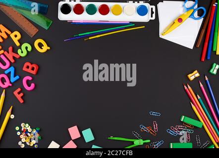 school supplies: multicolored wooden pencils, paper stickers, paper clips, pencil sharpener on a black chalk board, copy space, concept back to school Stock Photo