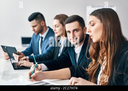 Portrait of smiling group of business people sitting in a row together at table in a modern office Stock Photo