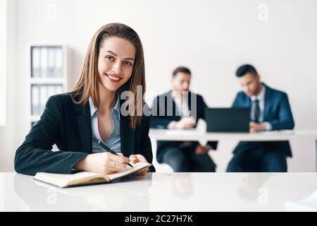 Happy smiling business woman portrait sitting in office and making notes with her business team on background Stock Photo