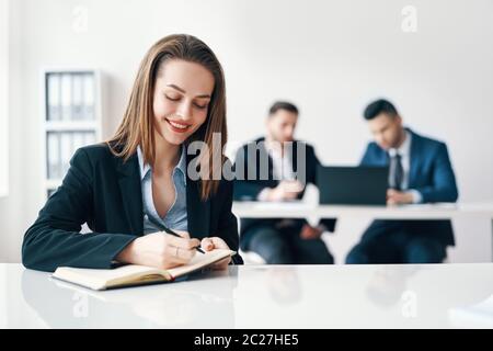 Beautiful smiling business woman writing and making notes in notebook in modern office Stock Photo