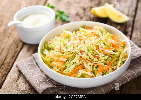 Coleslaw made of freshly shredded white cabbage and grated carrot in bowl, homemade mayonnaise-based salad dressing and lemon wedges in the back (Sele Stock Photo