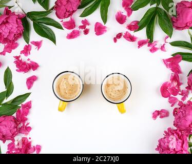 two yellow ceramic cups with coffee on a white table, next to a bouquet of red peonies, top view Stock Photo