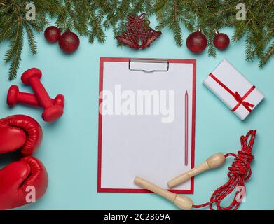 Dumbbells, boxing gloves,  blank  clipboard, gift, fir branches and Christmas ornament on green background. Top view with copy space. New Year, Christ Stock Photo