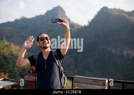 Asian man tourist is using a mobile phone to take a selfie for shared on social media, via social networking. Stock Photo