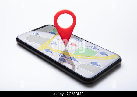 Close-up Of A Red Map Pin Pointer On Black Cellphone Over White Surface Stock Photo