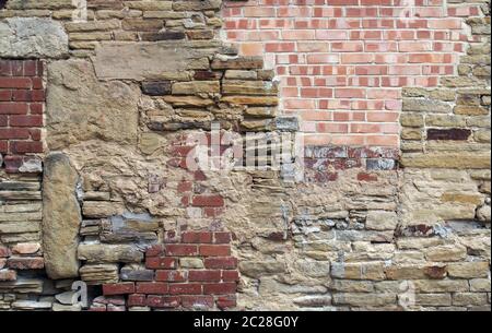 large old wall made of mixed bricks and stone with many jumbled patched and uneven repairs Stock Photo