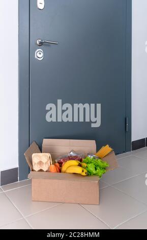 A box of food at the door. Home delivery food. Help to neighbors. Contactless delivery. Eggs, fresh vegetables and fruits on the house Stock Photo