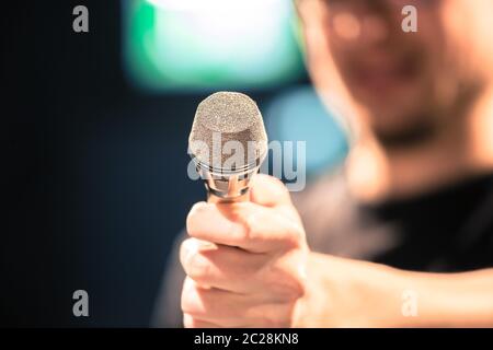 Speaker on the stage: Young Caucasian man is talking into a mirophone, blurry Stock Photo