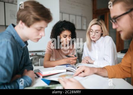 Portrait of two beautiful girl working together while sitting at the table in audience. Group of cool students studying with books and discussing new Stock Photo