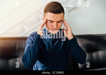 Young handsome man touching his temples, suffering from migraine, trying to concentrate on something, keeping eyes closed. At home. Stock Photo