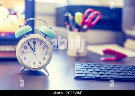 Alarm clock is standing on a grey desk, office stuff in the blurry background Stock Photo