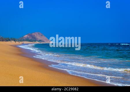 Wild Empty Tropical beach, vibrant yellow sand, bright blue sky, crystal clear waters with water crashing on the shore at daytime on a sunny day Stock Photo