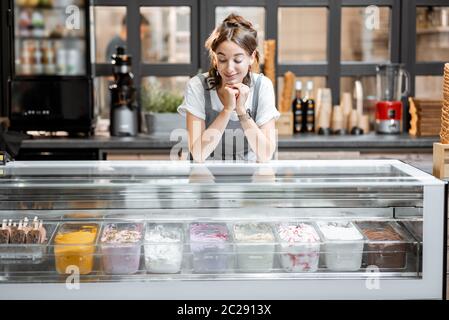 Portrait of a young and happy saleswoman at the counter in ice cream shop or cafe. Concept of a small business and retail Stock Photo