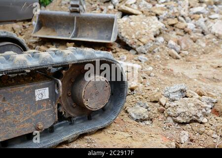 Rubber track of a mini digger in selective focus against background of concrete and earth excavation debris Stock Photo