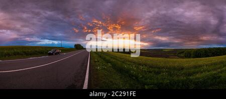 Spring rapeseed yellow fields, cloudy sunset evening sky, rural hills and regional road. Natural seasonal, travel, weather, countryside beauty concept Stock Photo