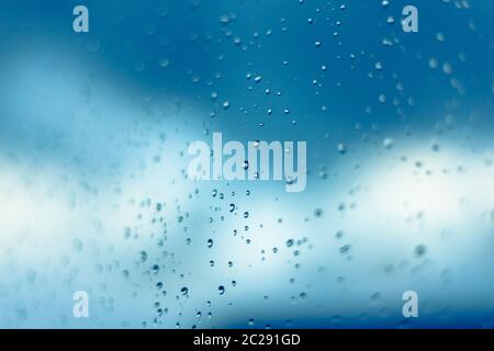 Water drops on the window, blue sky and clouds in the blurry background. Stock Photo