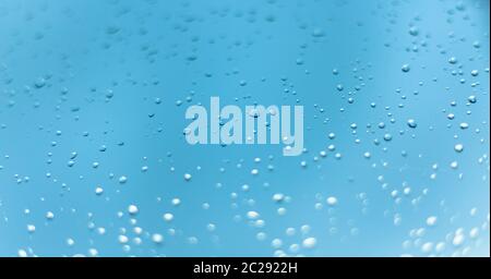 Water drops on the window, blue sky and clouds in the blurry background. Stock Photo