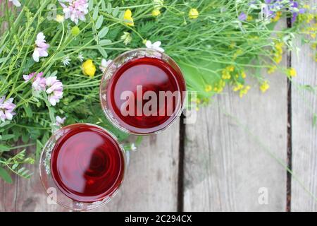 Midsummer night's dream strawberry elderflower cocktail, and wild blue and yellow flowers on the wooden board background. Two glasses of red wine Stock Photo