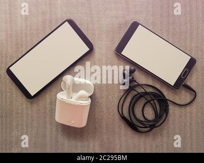 Comparison between two phones, one has 3.5mm jack wired headphones vs wireless earphones for music listening. Pros and cons, opposite contrary. Techno Stock Photo