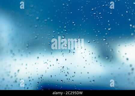 Water drops on the window, blue sky and clouds in the blurry background. Stock Photo