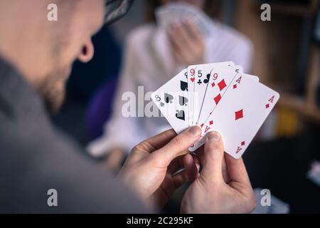Friends are playing cards together at home. Man is holding cards in her hands, woman in the blurry background. Stock Photo