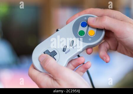 Hands are holding a retro video game controller and playing, blurry background Stock Photo