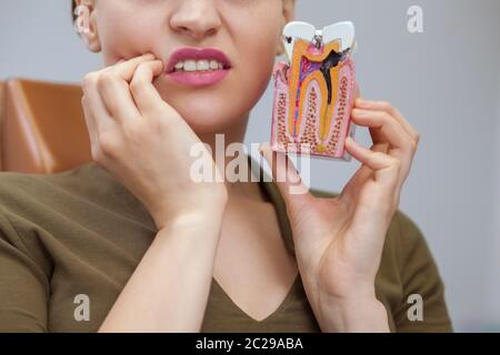 Cropped close up of a woman having toothache holding tooth mold with caries, copy space. Female patient waiting for dental treatment at the clinic. De Stock Photo