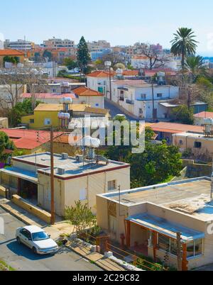 Aerial skyline of Paphos town in sunlight, car on road among houses of typical architecture, palms and green trees, Cyprus Stock Photo