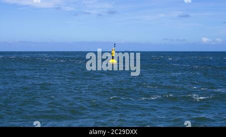 Gelbe Sicherheits-Boje schwimmt in der rauen Nordsee vor Horizont und blauem Himmel Stock Photo