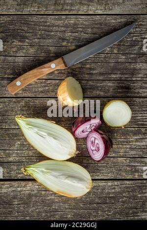 Halved fresh bulbs. Cut onions and knife on old wooden table. Top view. Stock Photo