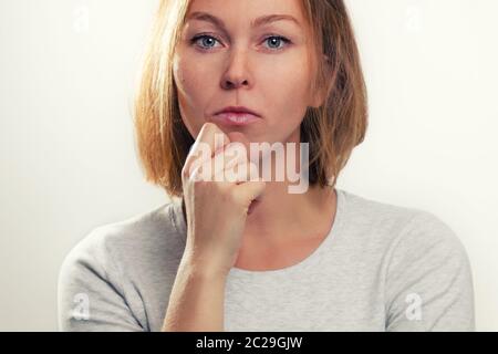 The concept of psychology and emotions. A young blonde woman leans her cheek on her hand, and looks thoughtfully. White background and close up. Stock Photo