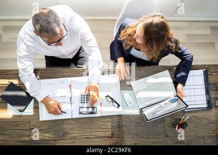An Overhead View Of Two Businesspeople Calculating Invoice In Office While Using Laptop Stock Photo